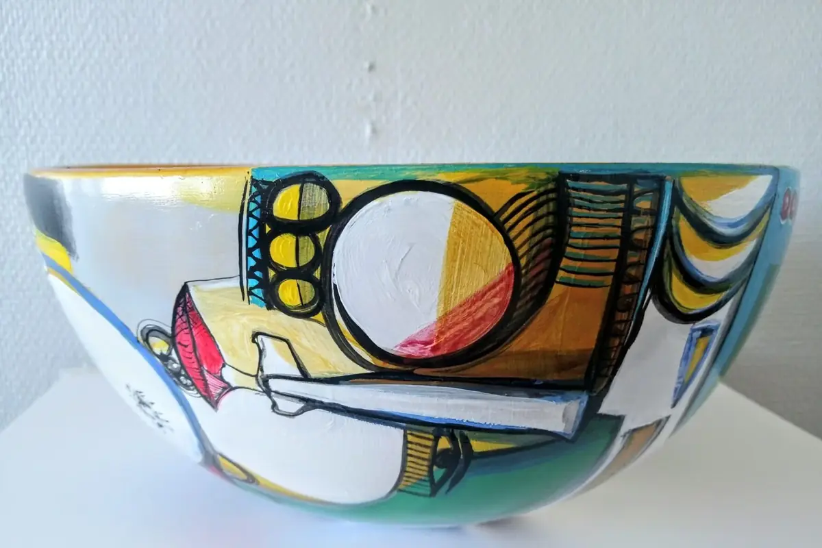 Painted bowl with circles, stripes and a hat shape in yellow, black and turquoise.