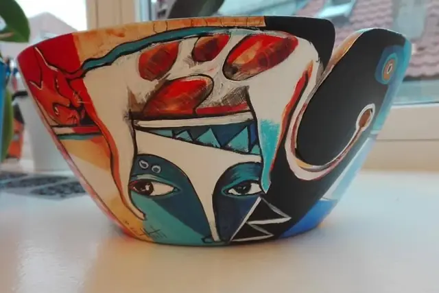Painted bowl with a mask-like face, red fruit and black curves.